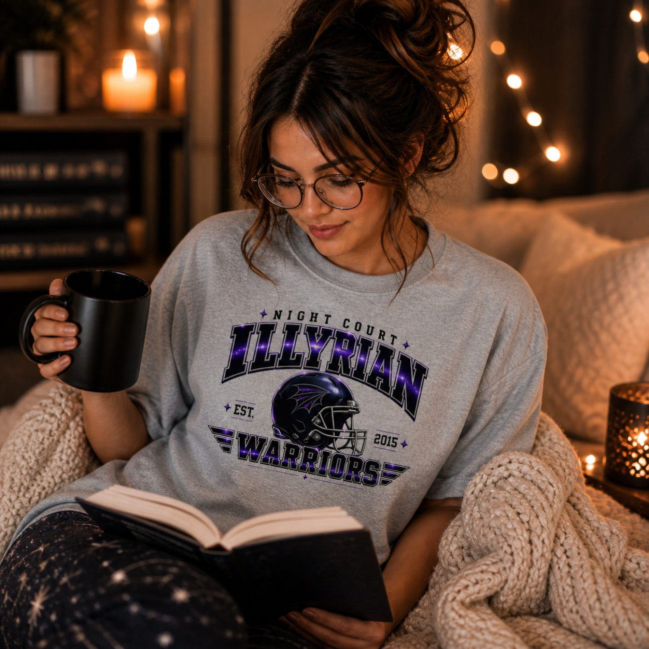 Woman wearing a sport grey Illyrian Warriors graphic t-shirt with a galaxy design, styled in a cozy bookish setting with soft lighting, candles, and a relaxed reading vibe.